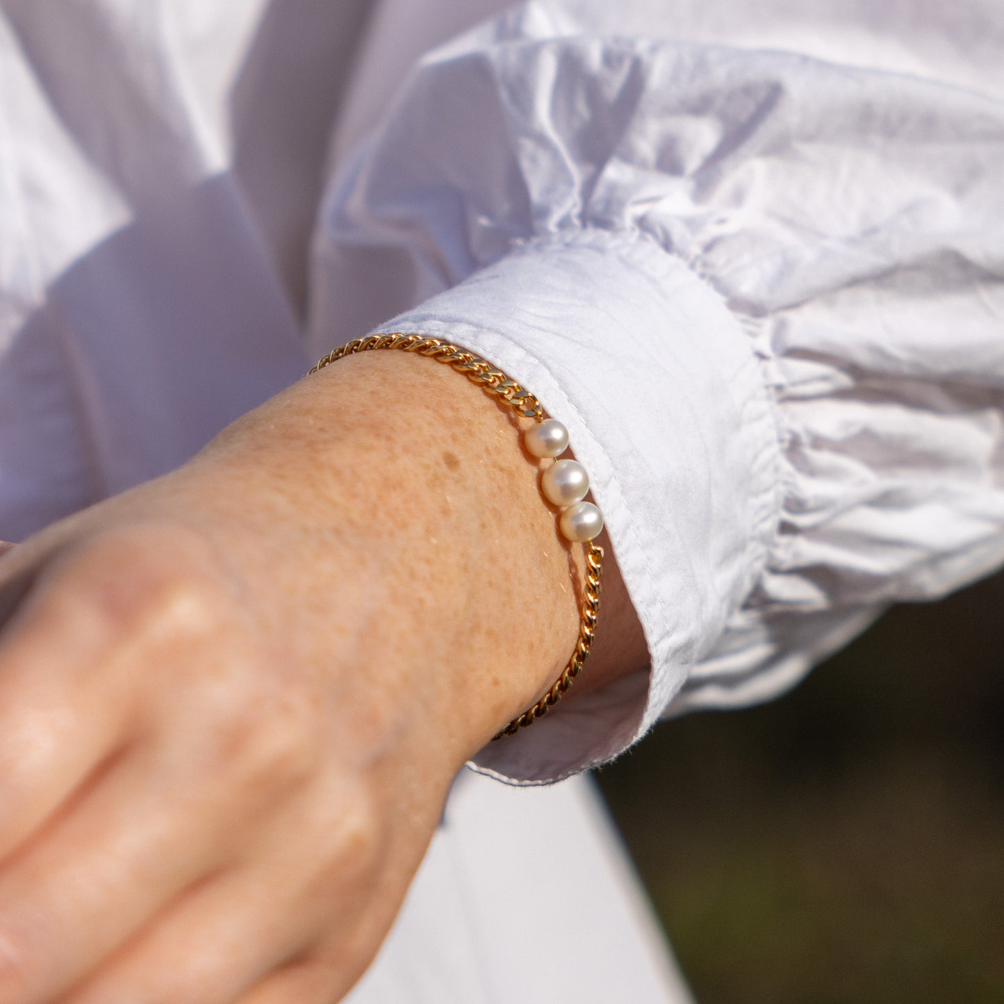 Gold Vermeil Bracelet with Three Freshwater Pearls, worn on womans wrist. The bracelet is siting below the cuff of a white shirt.