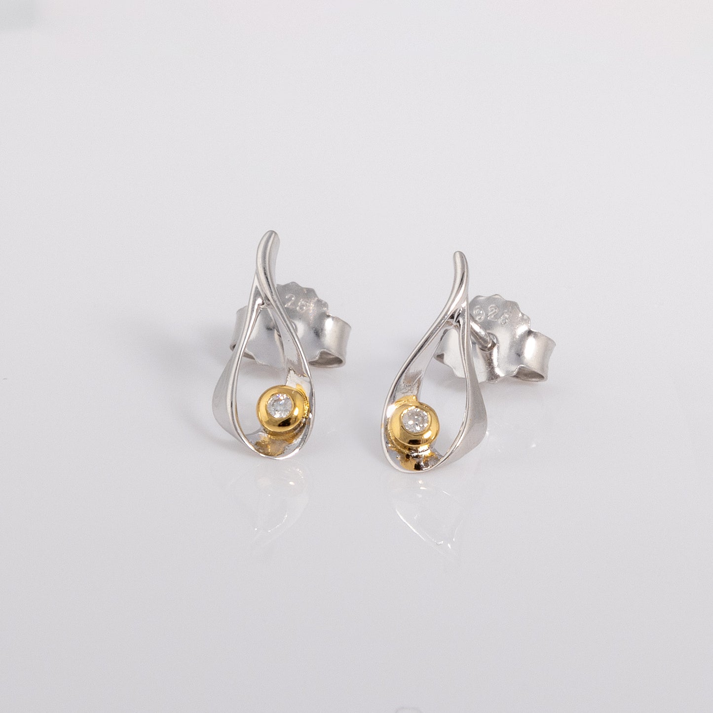 Stud earrings with a butterfly clasp. the earring is rhodium plated silver with gold vermeil detail surrounding one set diamond.