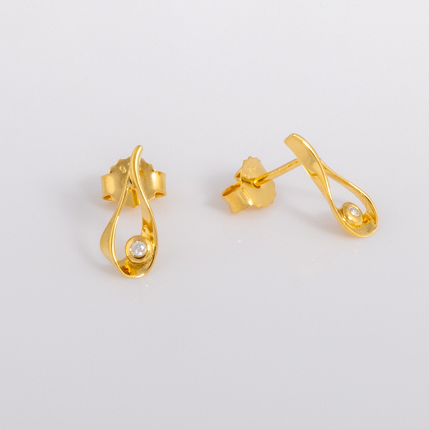 Gold vermeil stud earrings that feature a tear drop shape, detailed in a set diamond. The earrinsg have butterfly backs. One earring faces the lens and the other points off to the right.