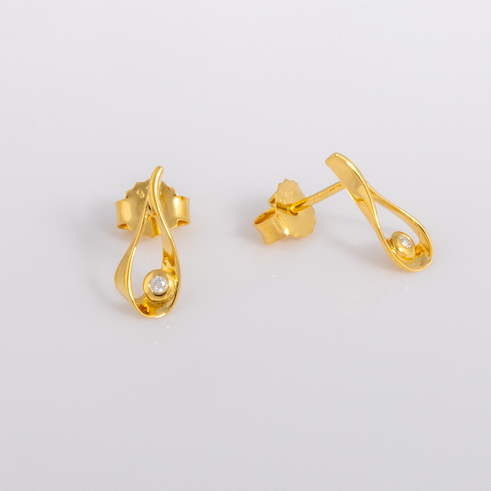 Gold vermeil stud earrings that feature a tear drop shape, detailed in a set diamond. The earrinsg have butterfly backs. One earring faces the lens and the other points off to the right.