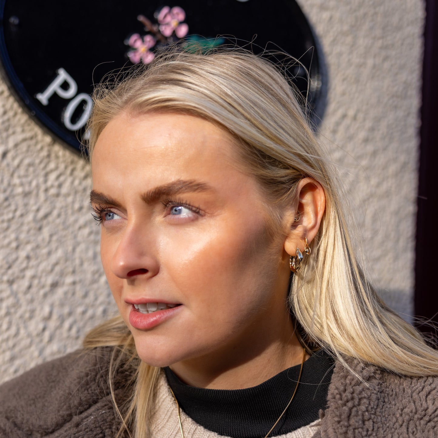 Model, a young blonde haired woman is wearing a tear drop shaped stud earring with a set diamond detail. The earring is gold vermeil with a butterfly clasp. The image is taken outside.