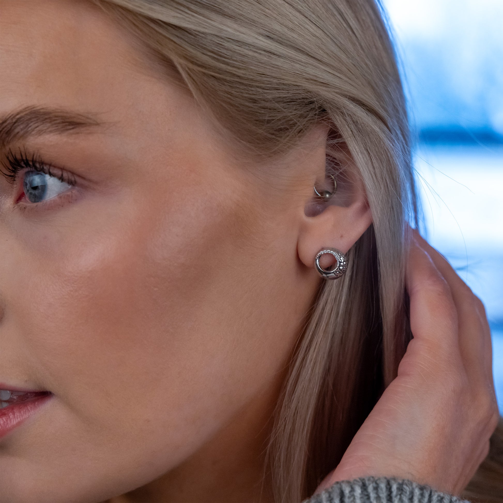 Side shot of model wearing rhodium plated silver Circle Stud Earrings with White Cubic Zirconia. The earrings have a textured finish and catch the light beautifully. Hypoallergenic, suitable for sensitive ears.