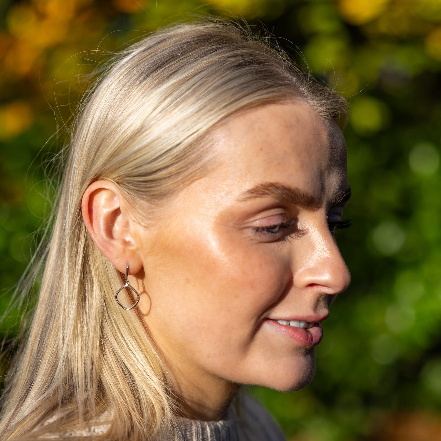 Simple Rhodium plated silver Hook Earrings. Catching and reflecting the daylight as worn outdoors by the model