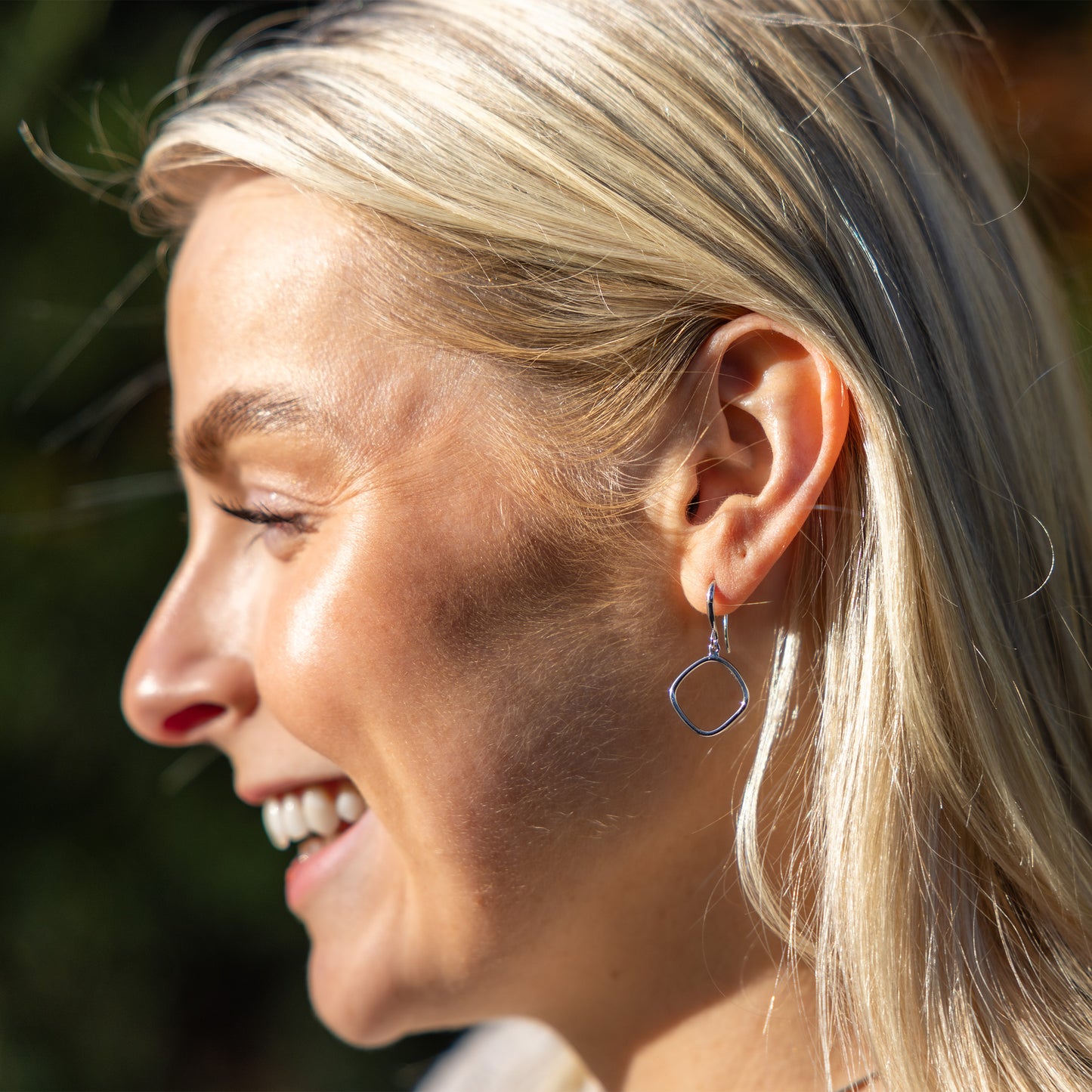 Simple Rhodium plated silver Hook Earrings worn on model outdoors. the earrings catch and reflect the sunlight