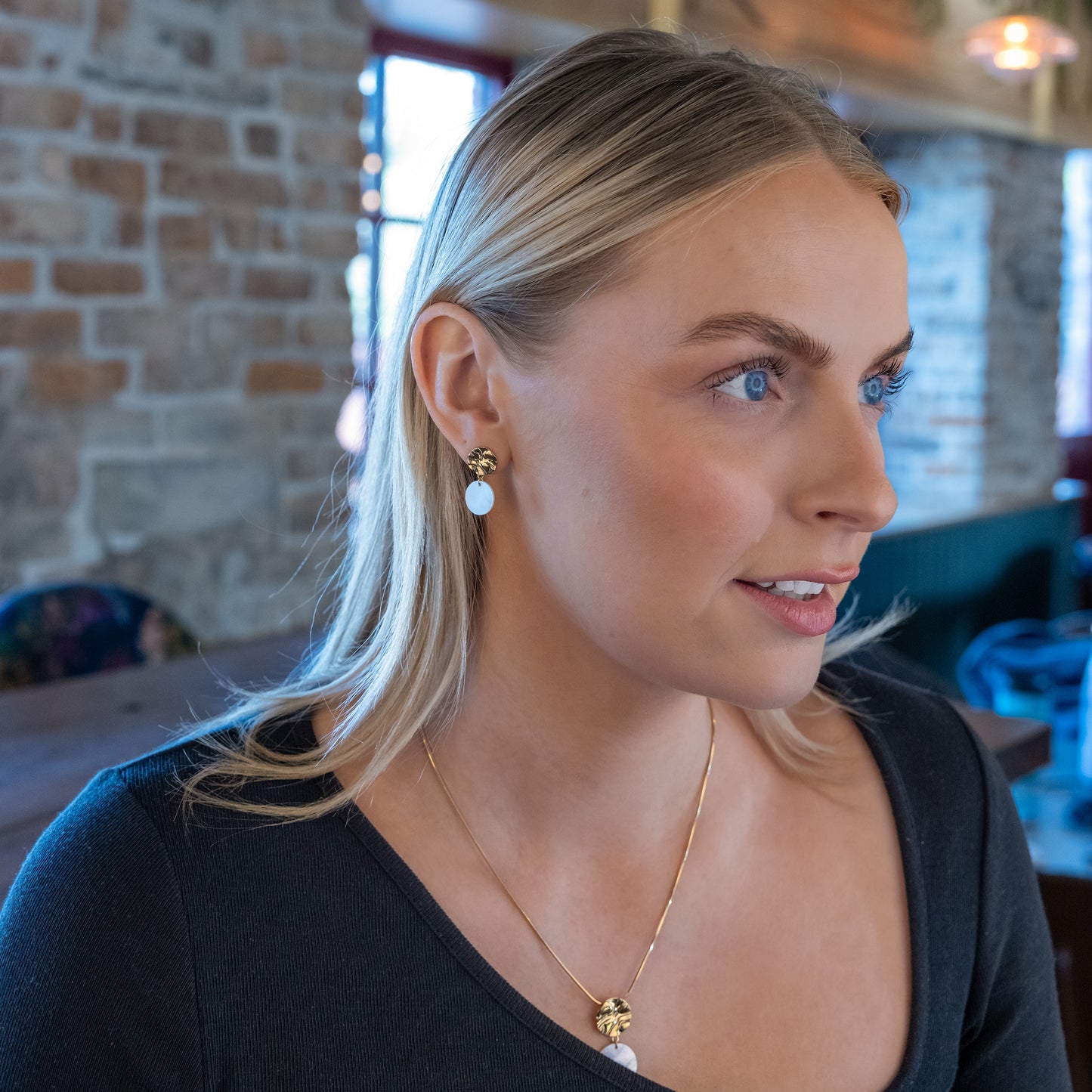 Model wearing gold vermeil and mother of pearl jewellery set. The stud earrings are gold vermeil with a molten texture and they have a dangling mother of pearl disc.