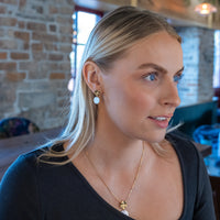 Model wearing gold vermeil and mother of pearl jewellery set. The stud earrings are gold vermeil with a molten texture and they have a dangling mother of pearl disc.
