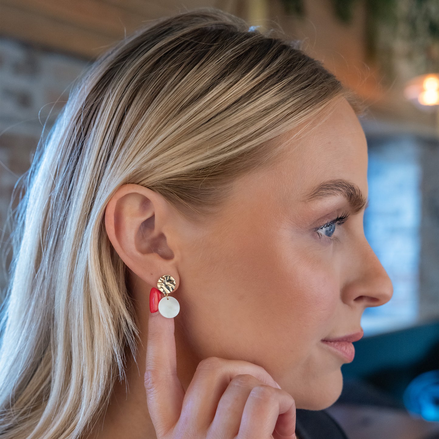 Model turning head to side, showing her molten textured stud earrimgs with a disc of mother of pearl dangling.