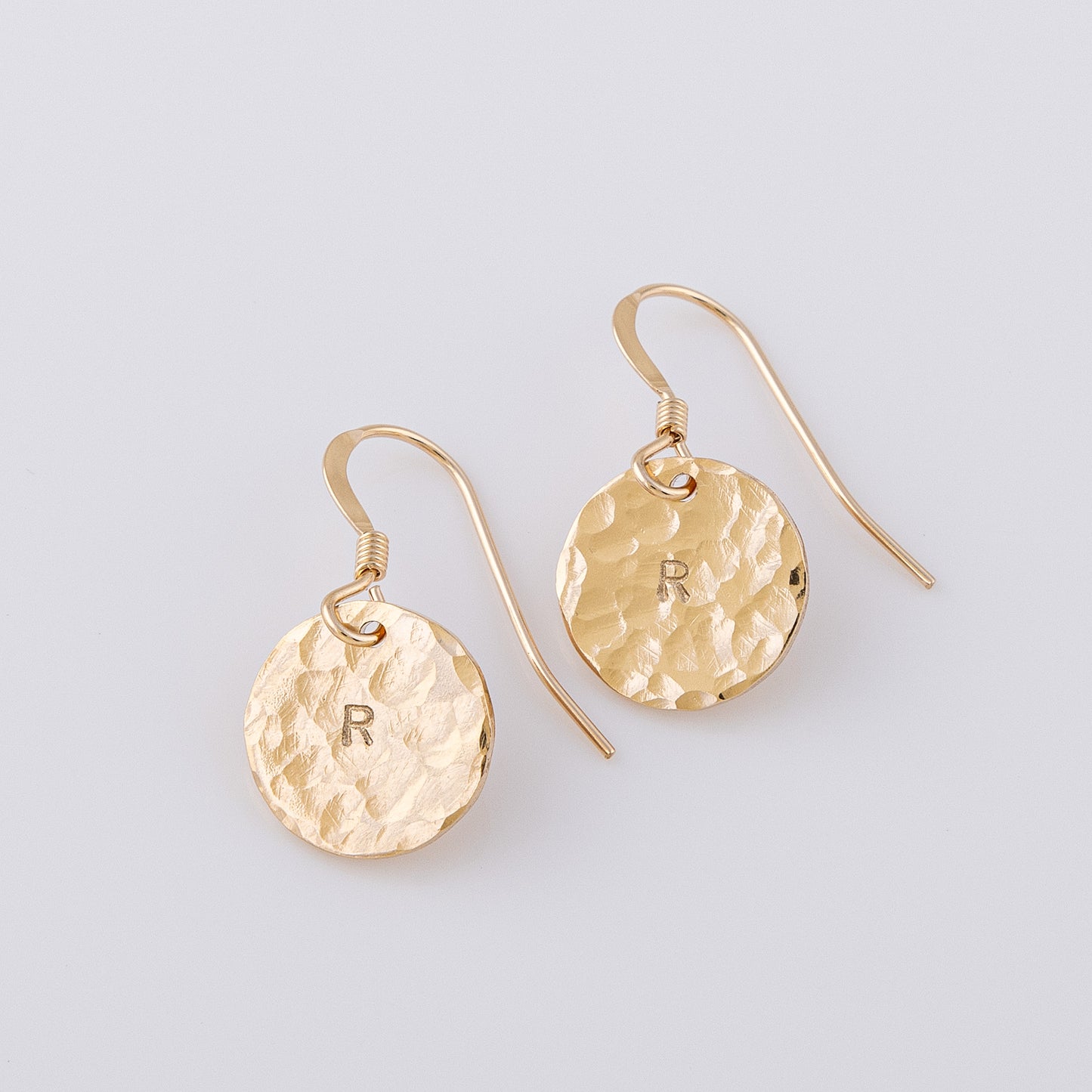Hammered 14ct gold-filled disc earrings. The fish hook earrings have a letter R stamped in the centre of the disc. The textured finish creates a stunning sparkle when they catch the light.
