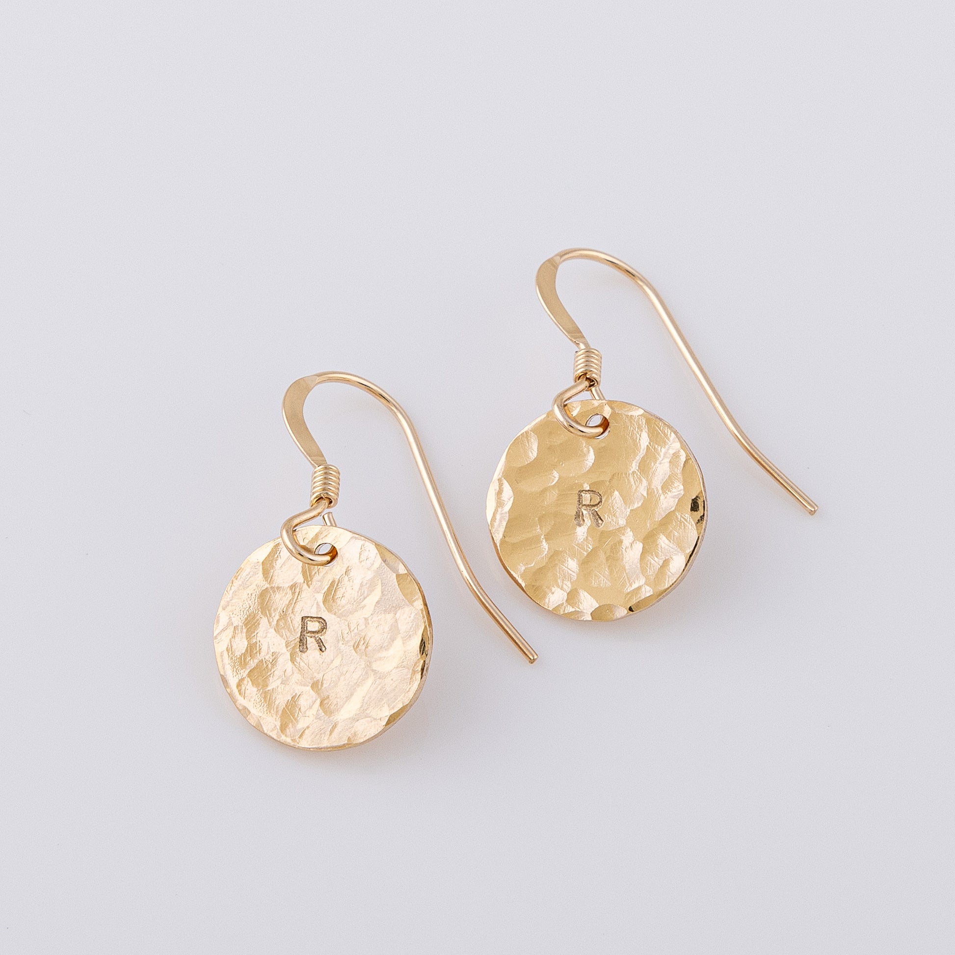 Hammered 14ct gold-filled disc earrings. The fish hook earrings have a letter R stamped in the centre of the disc. The textured finish creates a stunning sparkle when they catch the light.