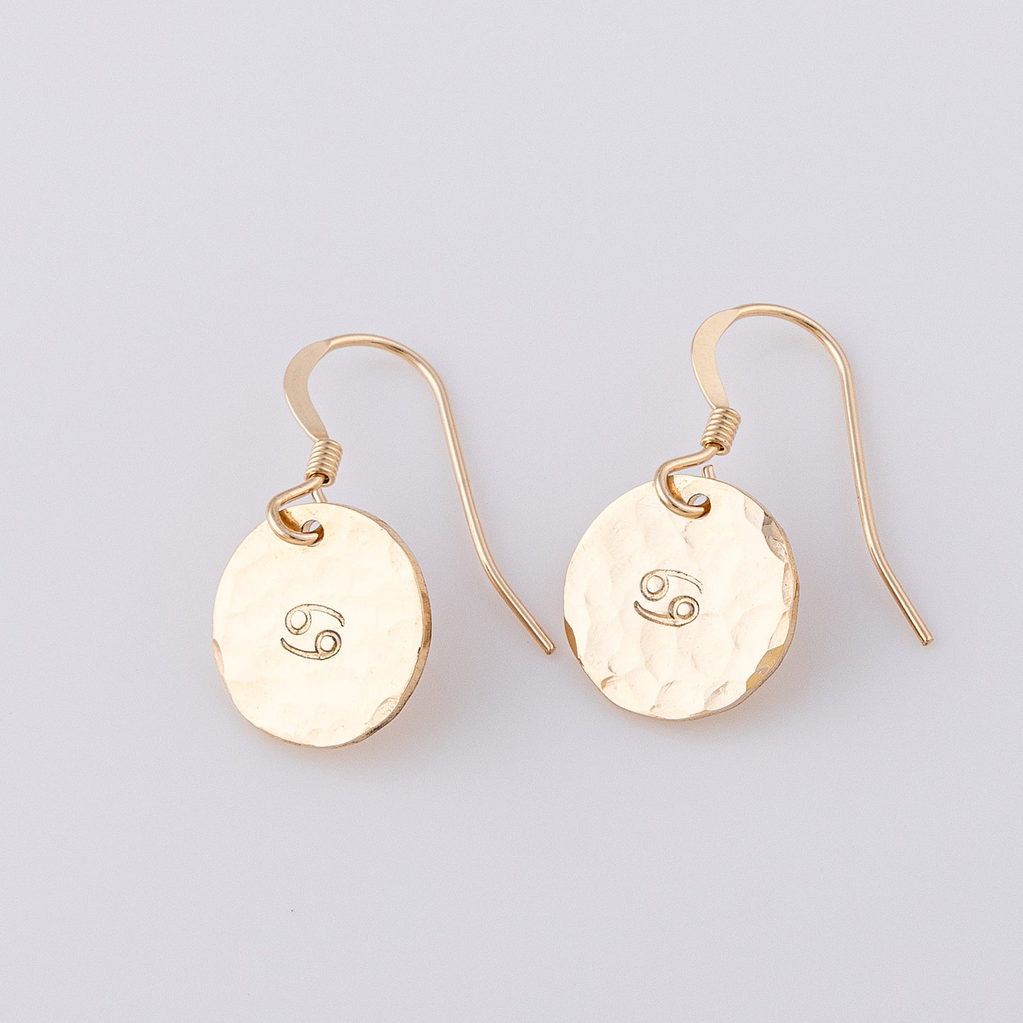 Fish hook, star sign earrings hand made from 14ct gold-fill. They have a hammered disc stamped with the cancer star sign stamped in the centre.