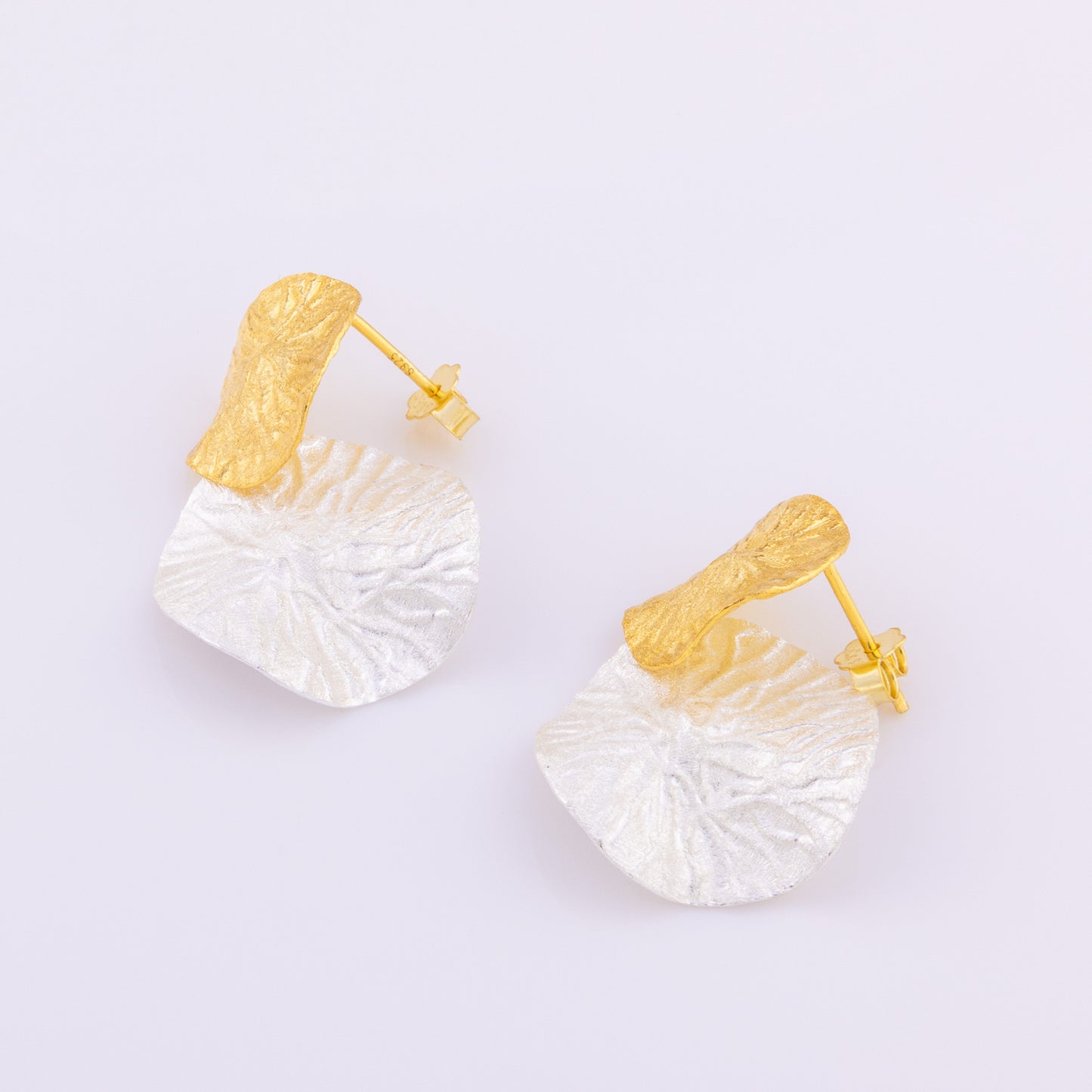 Large, statement earrings. Two dangling, leaf textured discs, one coming after the other. The top disc is gold vermeil while the lower disc is rhodium plated silver. The earrings are studs with a butterfly back, tarnish resistant and hypoallergenic.