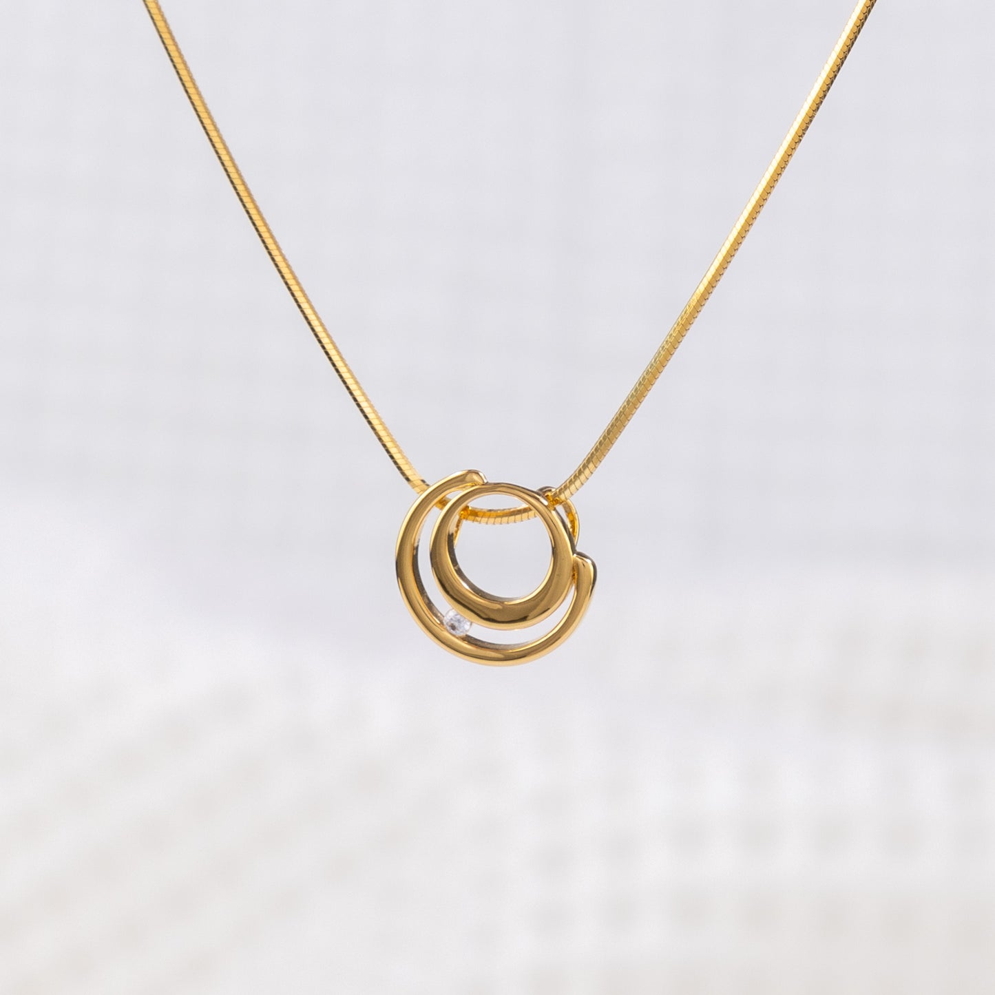 Close up of a gold vermeil circle shaped pendant necklace with white cubic zirconia detail on a delicate snake chain. White background on image