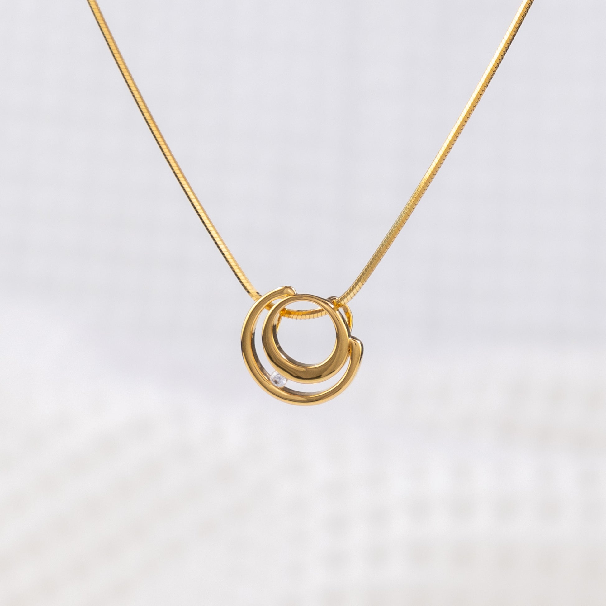 Close up of a gold vermeil circle shaped pendant necklace with white cubic zirconia detail on a delicate snake chain. White background on image