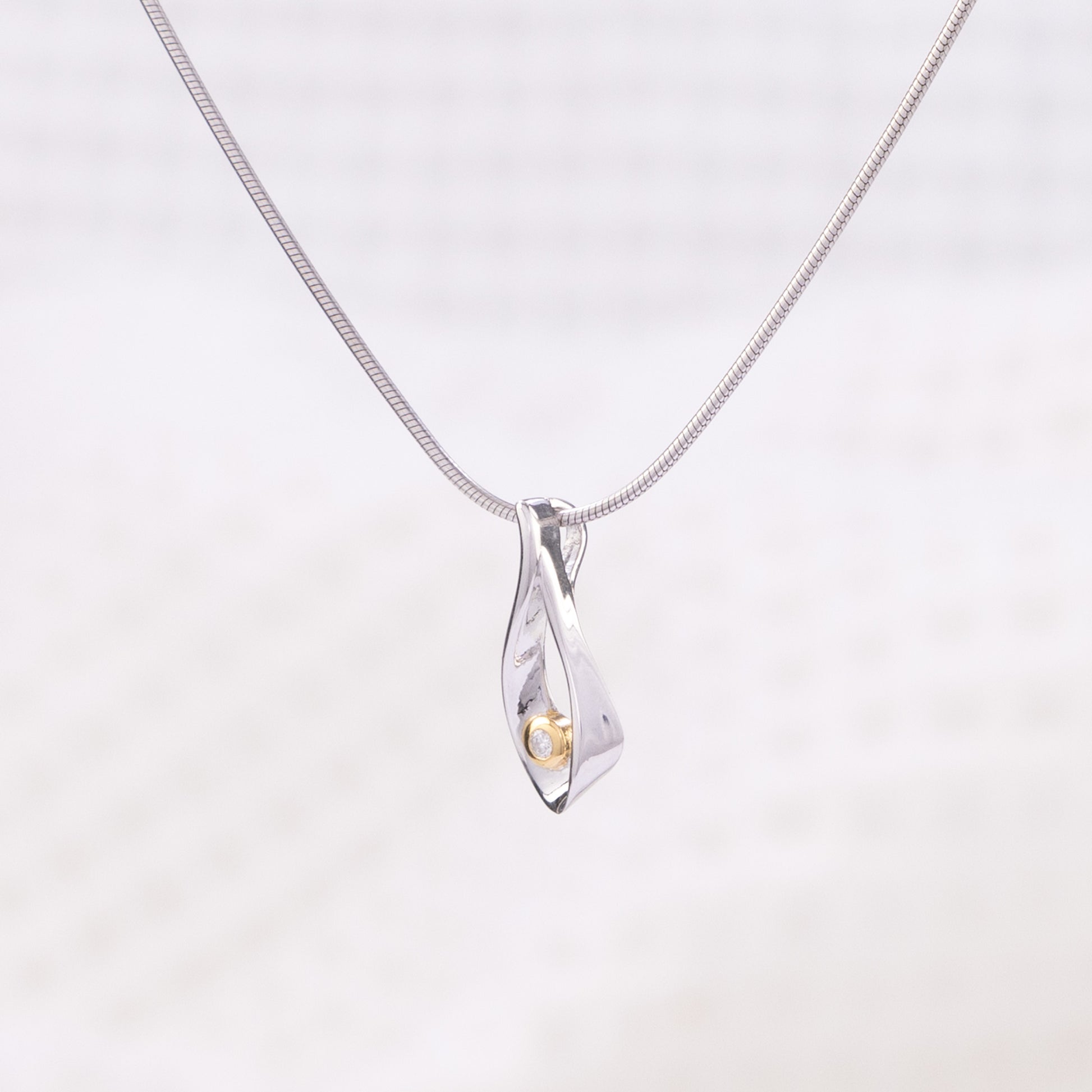 Side angle of a rhodium plated silver, snake chain, pendant necklace. The tear drop pendant is rhodium plated silver with gold vermeil detail surrounding a single set diamond.