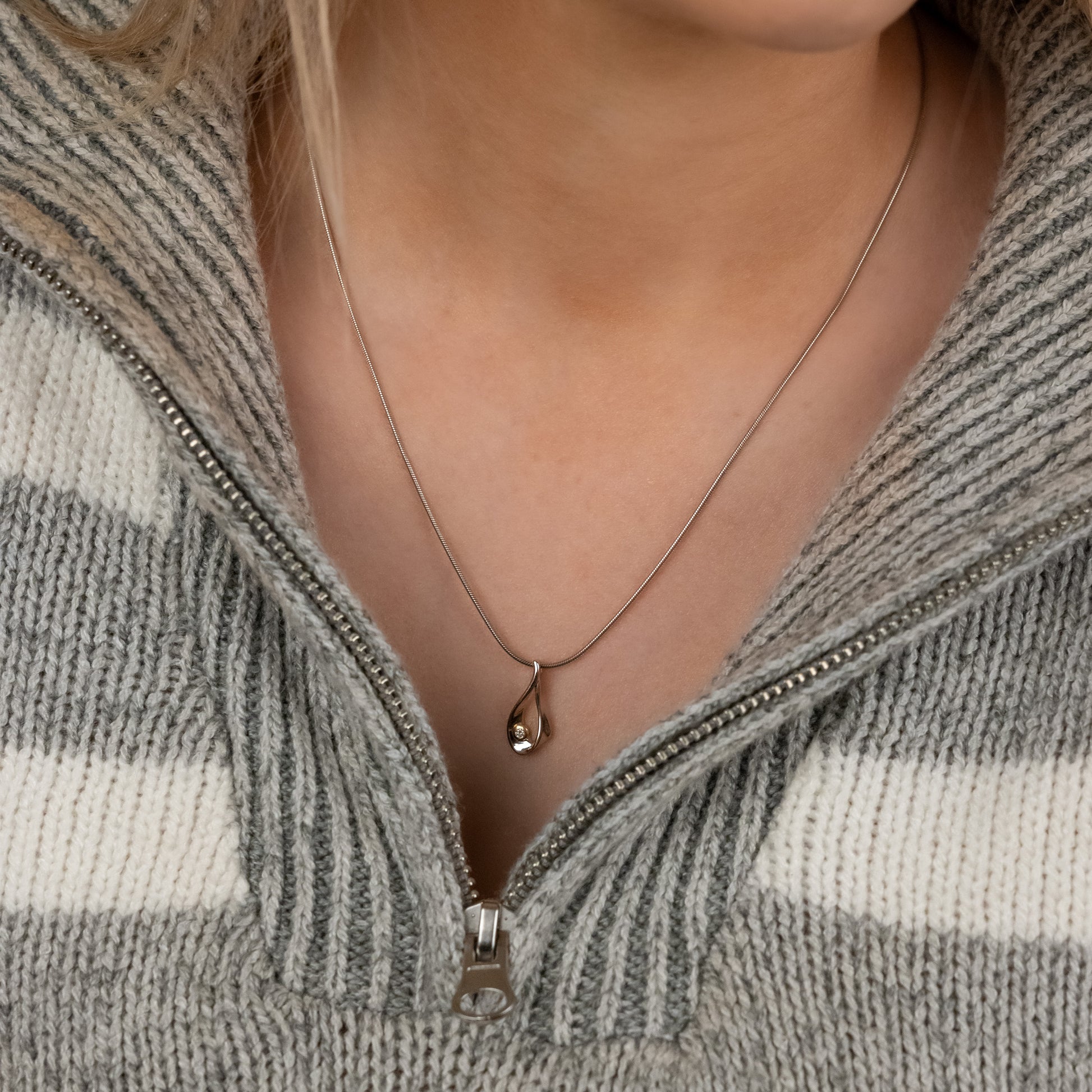 Rhodium plated silver pendant necklace worn aginst bare skin. Model is wearing a jumper zipped down a quarter of the way. The pendant is rhodium plated silver with gold vermeil detail surrounding a single set diamond. The chain is a rhodium plated silver snake chain with a lobster clasp.