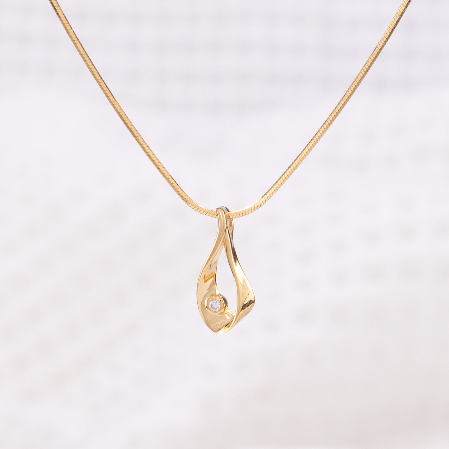 A gold vermeil pendant necklace, with a gold vermeil snake chain. The pendant is a tear drop shape with a set diamond detail.