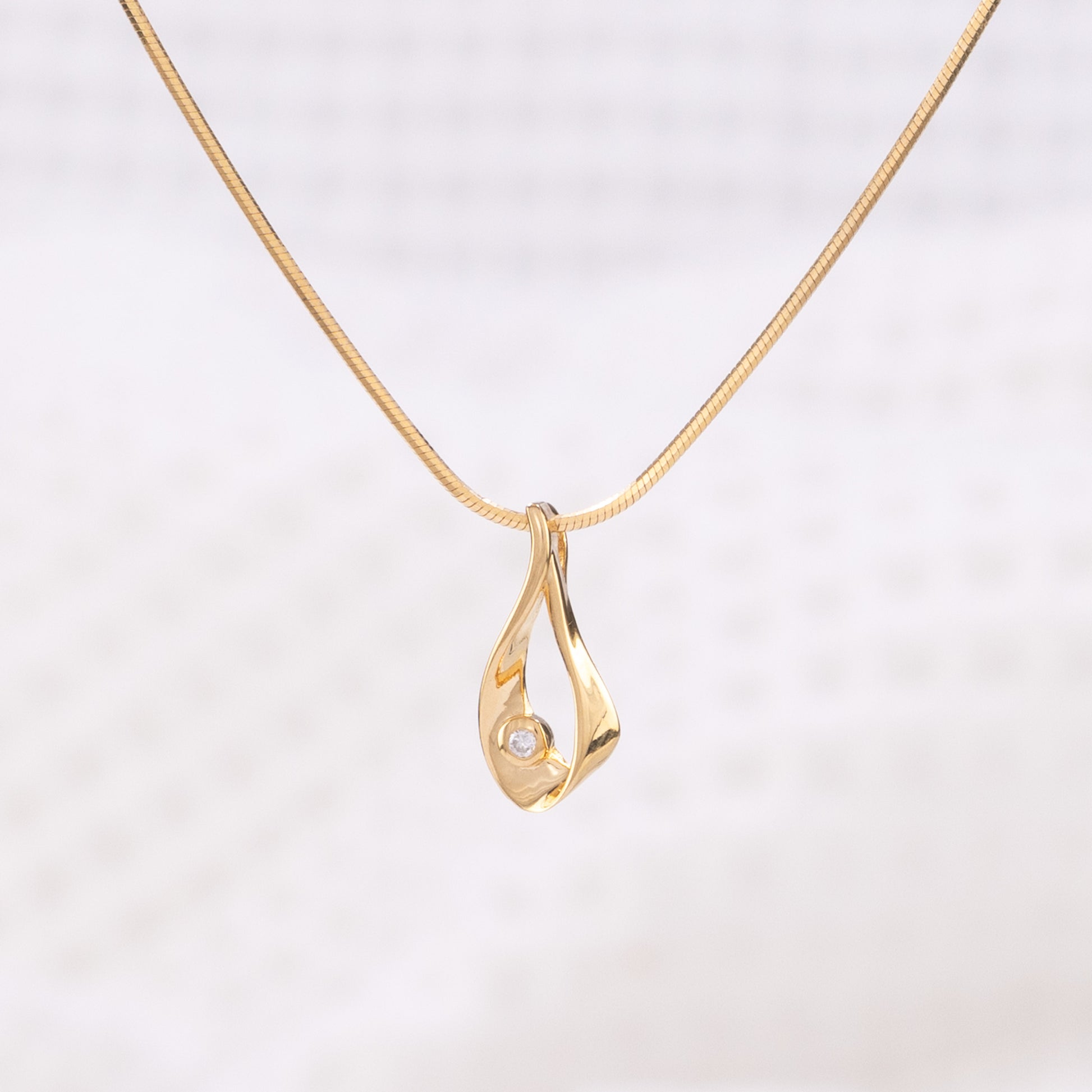 A gold vermeil pendant necklace, with a gold vermeil snake chain. The pendant is a tear drop shape with a set diamond detail.