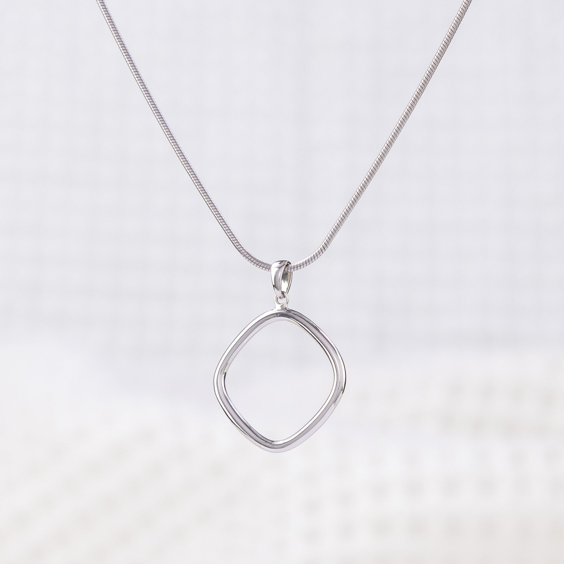 Simple Rhodium pkated silver Pendant Necklace. The silver reflects light and shines. The pendant hangs upon a snake chain