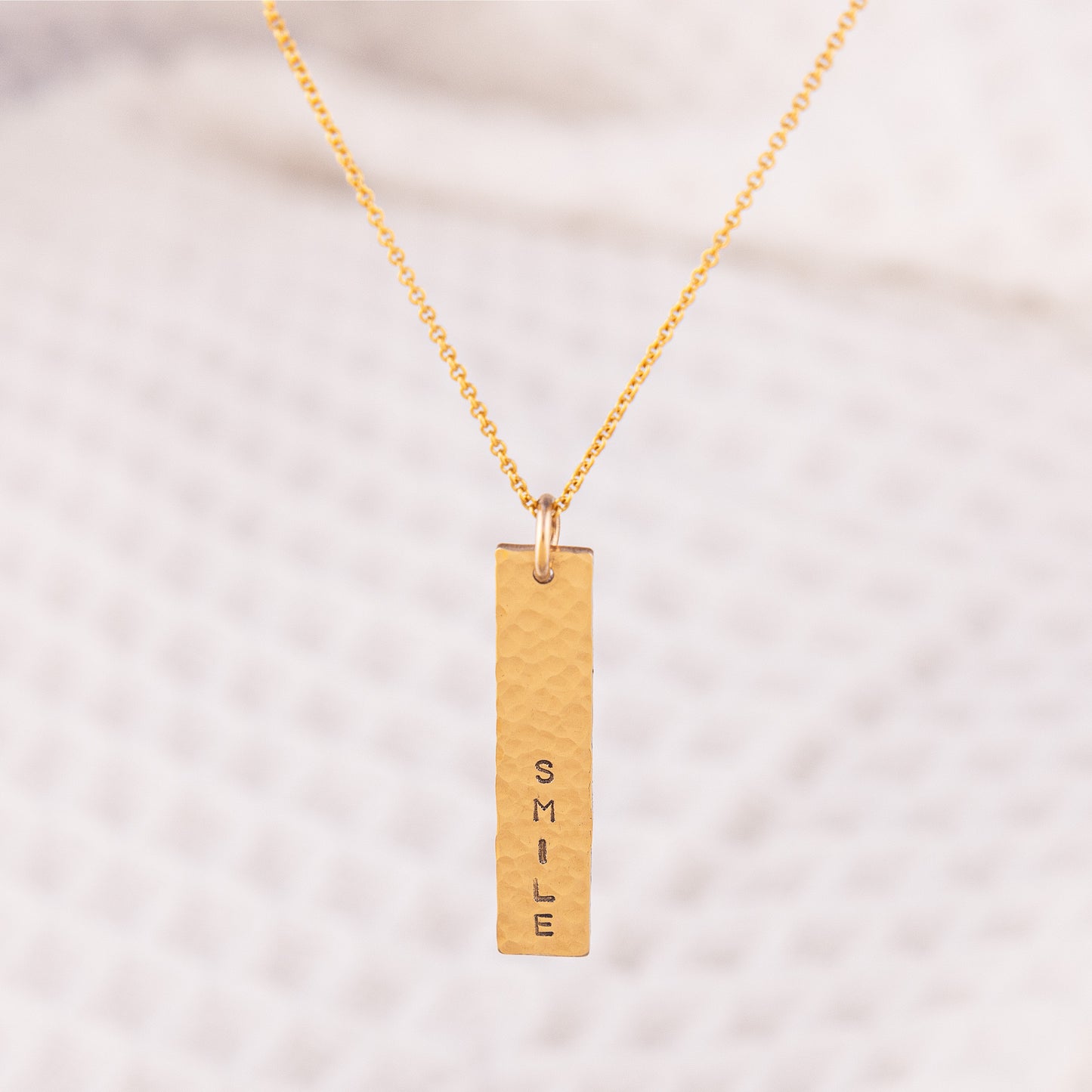 A personalsied 14ct gold fill necklace. The hammered bar pendant is hand stamped with a custom word of your choice.