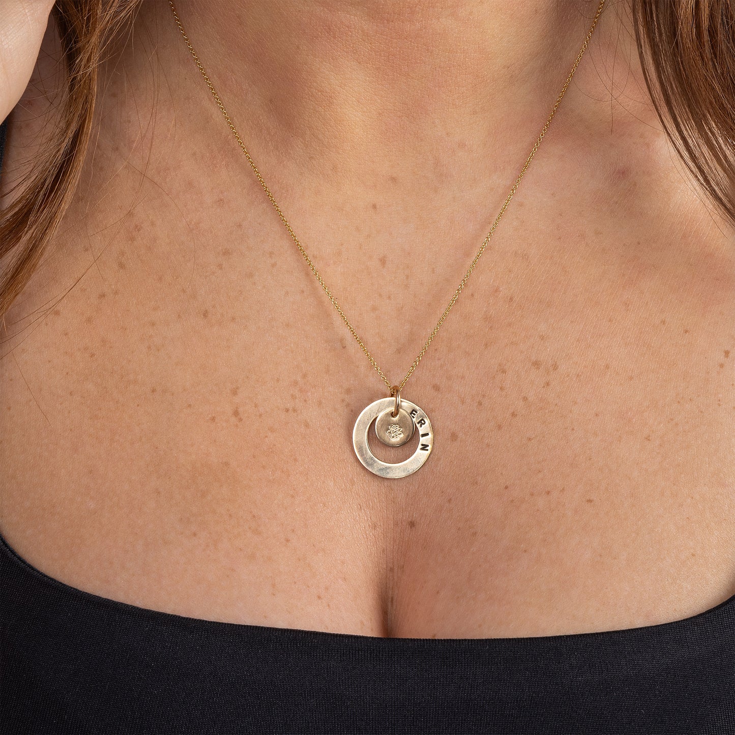 Model earing a personalised, 14ct gold filled necklace. The necklace pendant has a smooth textured halo, stamped with your name and a small smooth disc in the centre of the halo, stamped with your birth flower.