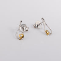 Rhodium plated silver stud earrings that have a tear drop shape. They have a gold vermeil detail and a set diamond in each earring. They hvae a butterfly clasp. One earring is facing the camera, while the other tilts off to the right