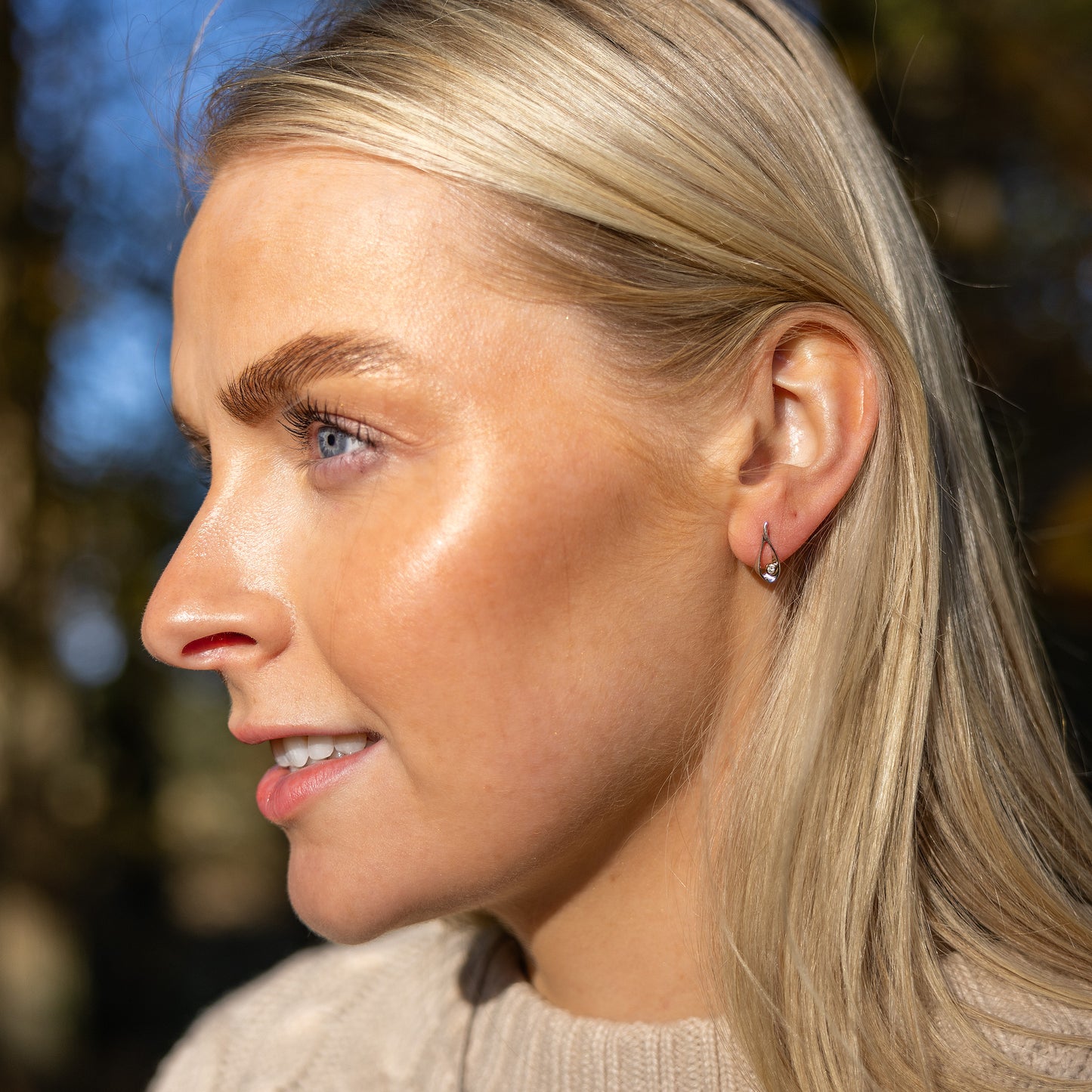 Model, young blonde haired woman, wearing rhodium plated silver stud earrings that have a gold vermeil detail surrounding one set diamond. The earrings have a butterfly clasp and are a tear drop shape.