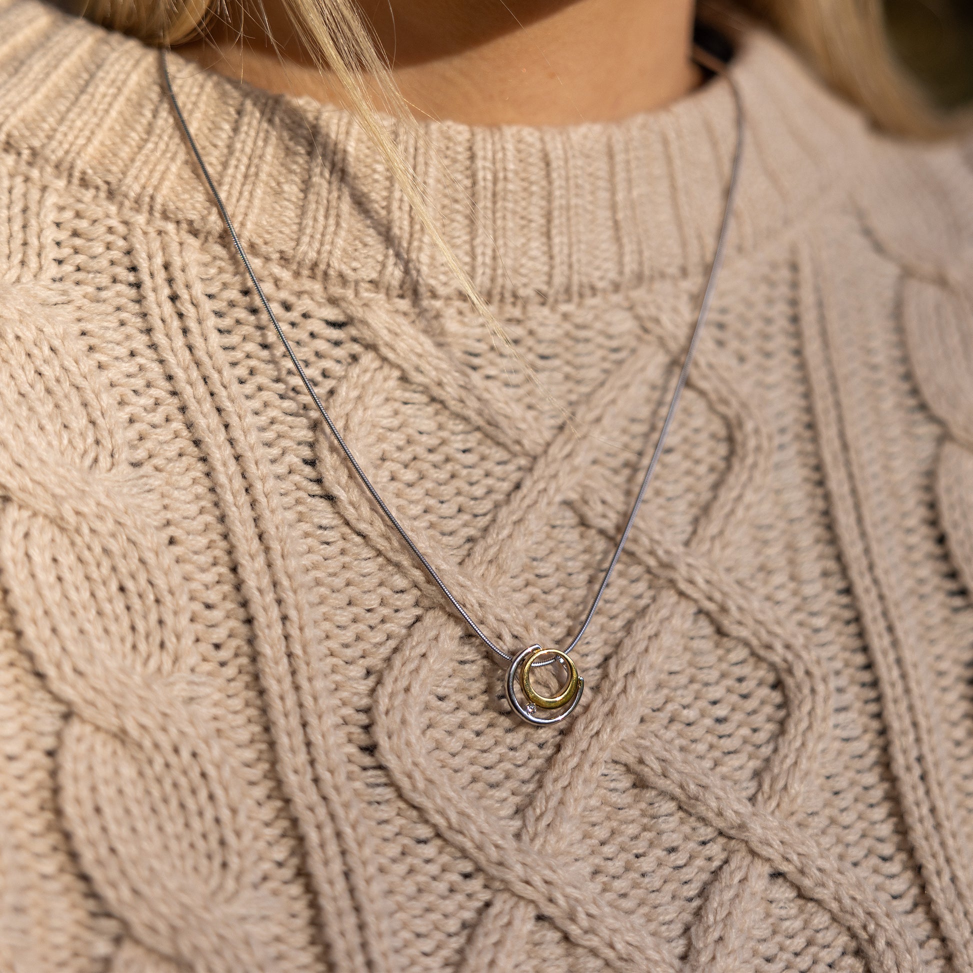 Gold vermeil and rhodium plated silver necklace with white cubic zirconia detail. The pendant has a circle design and sits on a rhodium plated silver, snake chain. The necklace is worn on top of a beige aran jumper with a round neck. 