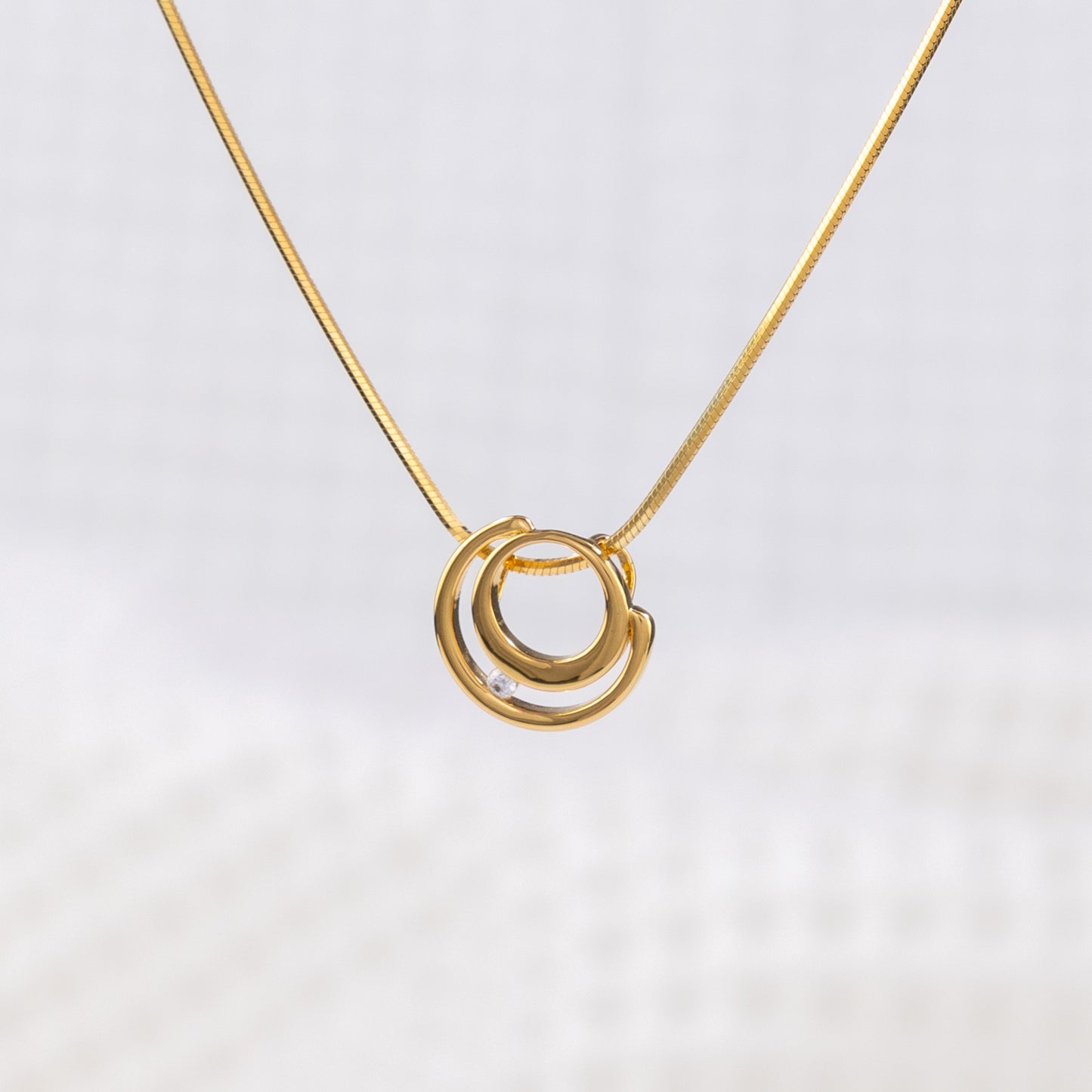 Close up of a gold vermeil circle shaped pendant necklace with white cubic zirconia detail on a delicate snake chain. White background on image 