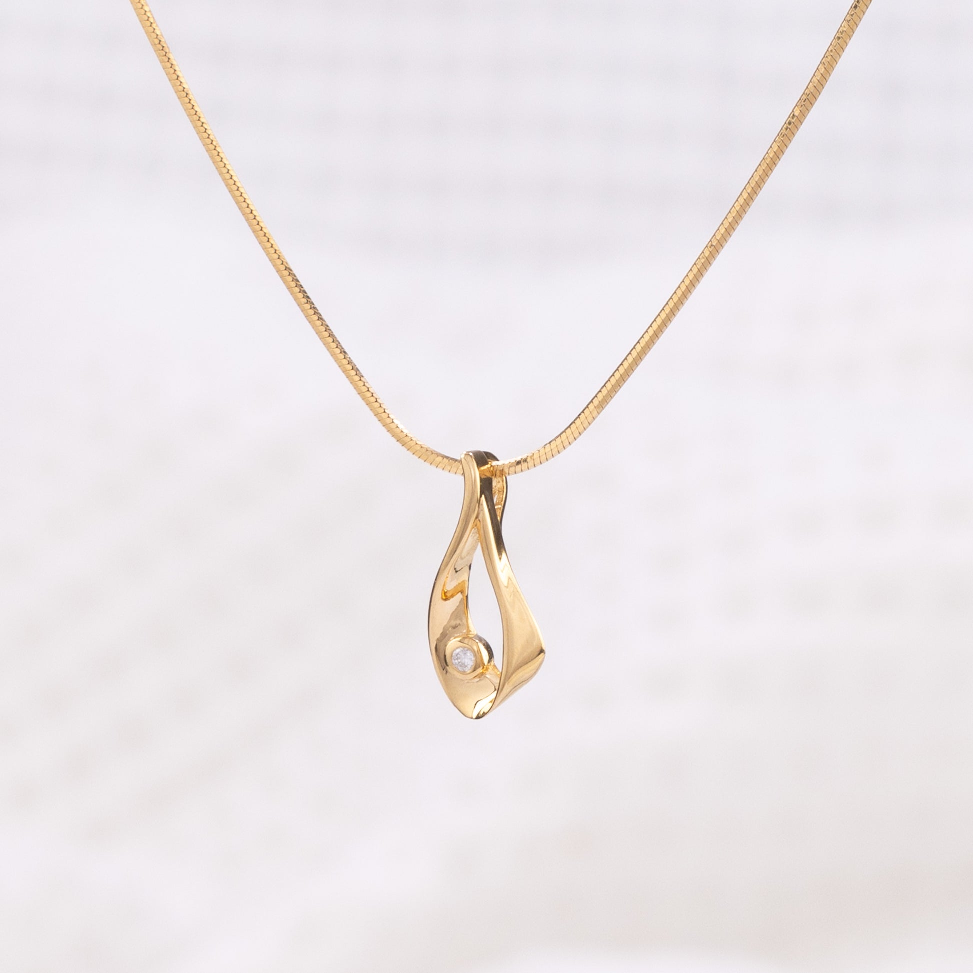 A side angle of a gold vermeil pendant necklace. The pendant takes a tear drop shape and is detailed with a set diamond. The chain is a gold vermeil snake chain. The necklace is photographed on a white background.