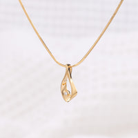 A side angle of a gold vermeil pendant necklace. The pendant takes a tear drop shape and is detailed with a set diamond. The chain is a gold vermeil snake chain. The necklace is photographed on a white background.