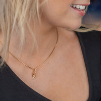 A gold vermeil pendant necklace on a young woman wearing a asymetrical neckline black top. The pendant is a tear drop shape with a set diamond detail. The chain is a gold vermeil snake chain