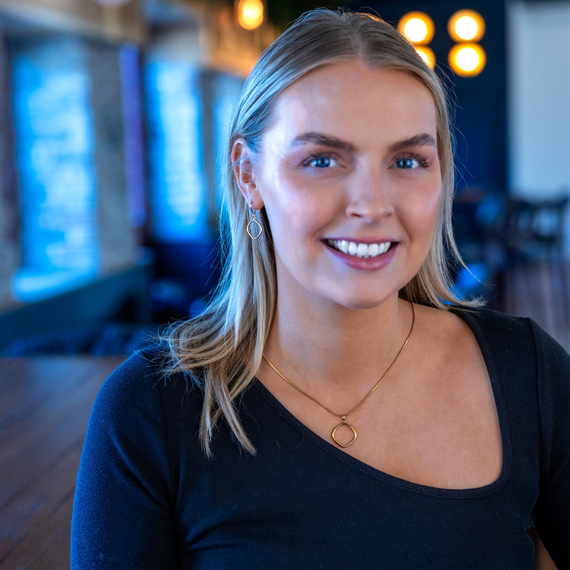 Model smiling at camera in matching jewellery set. The set has a simple, rounded edge, geometric shape pendant. The necklace and earrings are gold vermeil, hypoallergenic and tarnish resistant