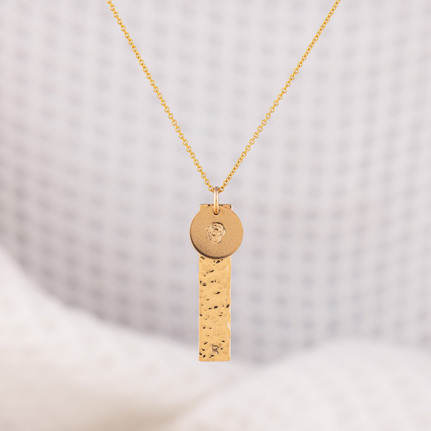 14ct Gold-filled gold necklace featuring a hammered rectangular pendant stamped with an initial and a round disc pendant stamped with a flower