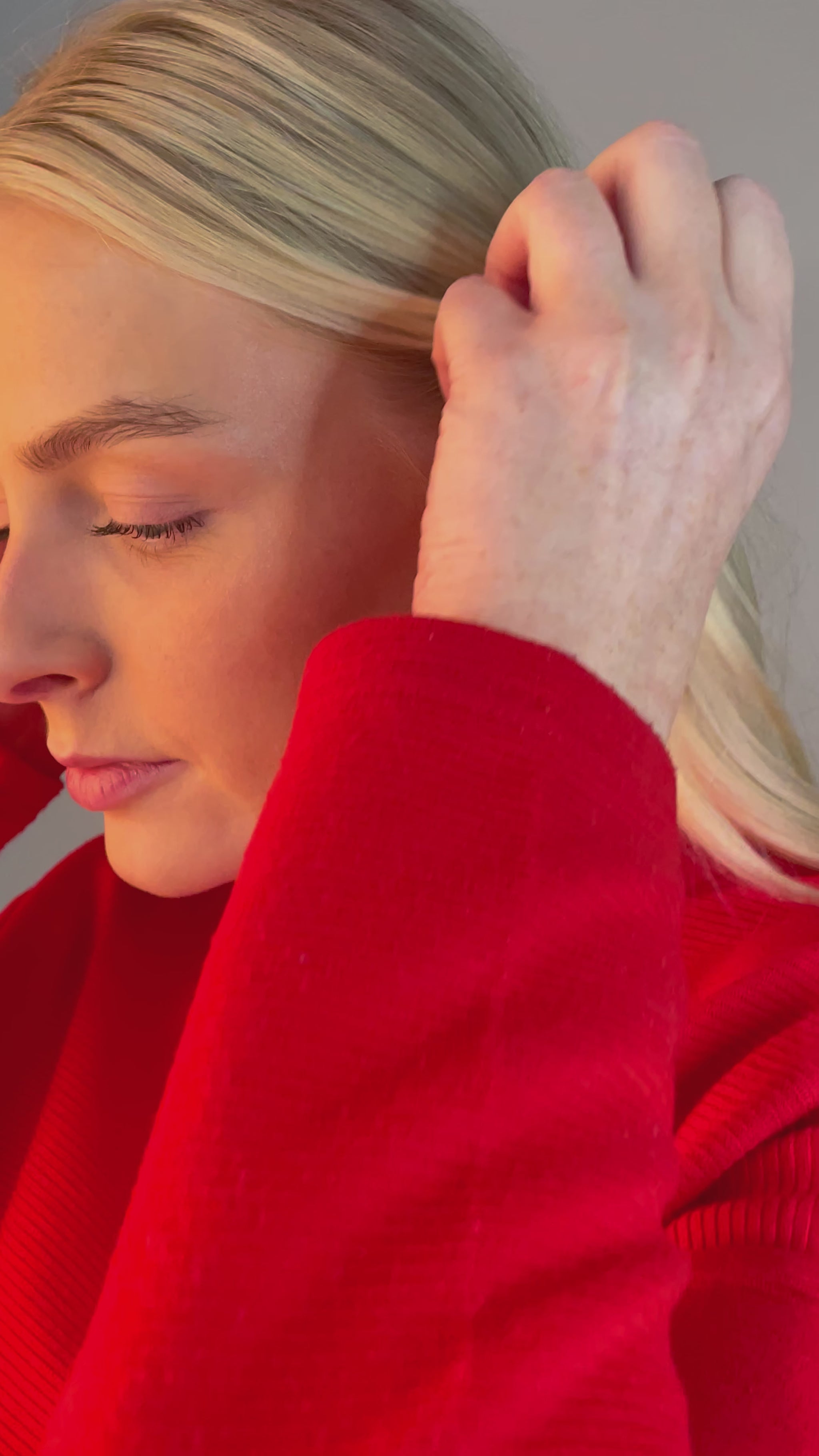 Video of model, young blonde haired woman, showing her stud earring in her ear. The earring is rhodium plated siilver with gold vermeil detail surrounding a set diamond. They are tear drop shaped with a butterfly clasp. The model has cherry red nails and is wearing a bright red top.